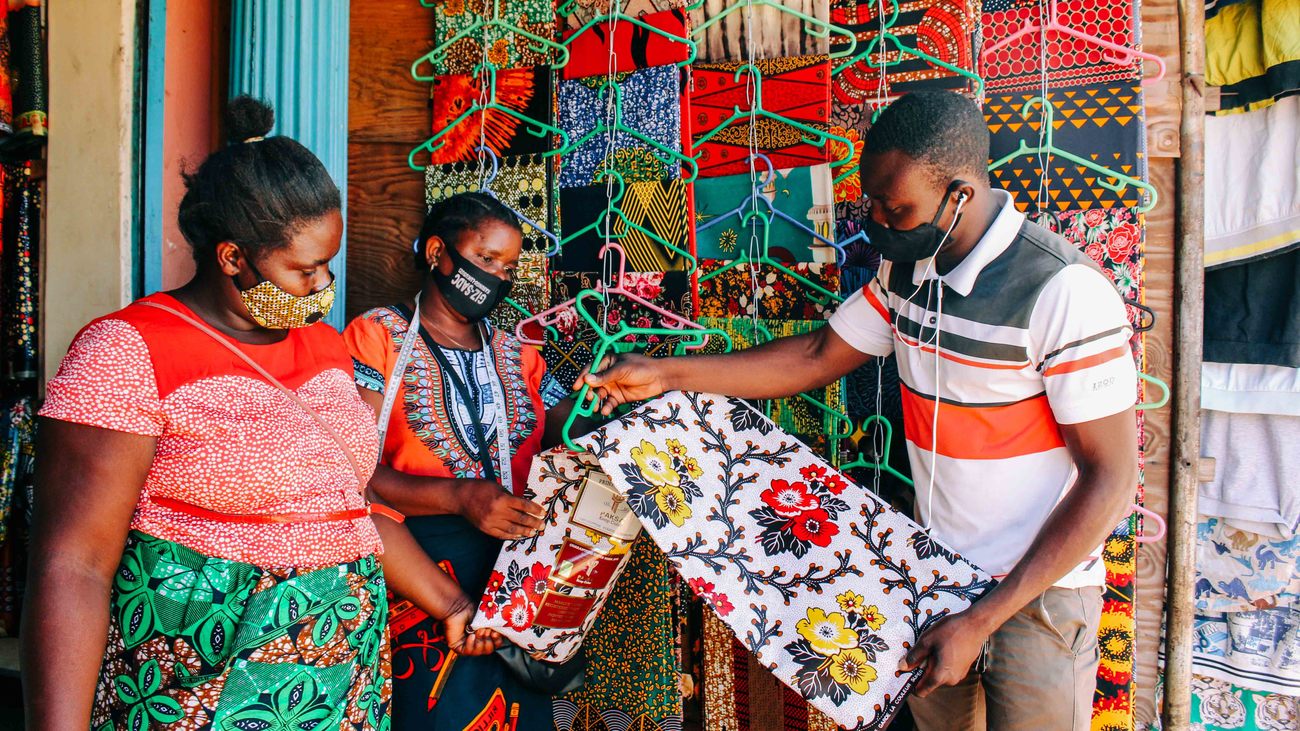 Two women from the Lifupa Women's Group pick out colorful textiles from a male shop vendor 