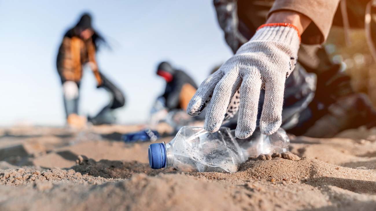 A hand reaches to pick up a plastic bottle on the beach. IFAW encourages all of us to do our part in reducing plastic pollution. 