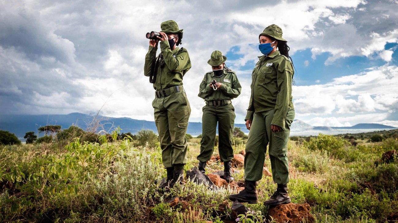 In der Nähe eines Ranger- Stützpunkts im Amboseli-Ökosystem in Kenia: Beatrice Sailepu, eine vom IFAW geförderte Olgulului- Wildtier-Community-Rangerin (OCWR) des Team Lioness, mit Fernglas. Daneben Anastacia Kupayi und Eunice Peneti (mit GPS).