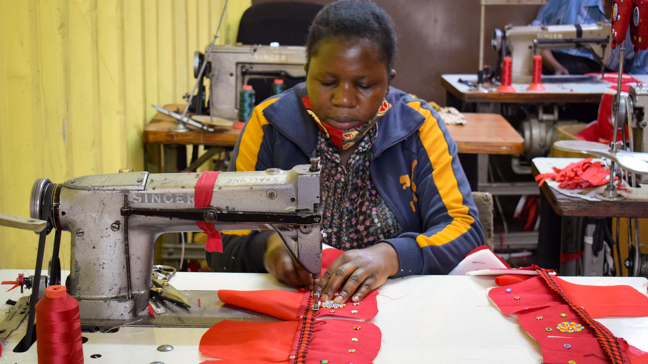 Een medewerkster van een door IFAW ondersteunde leverancier zit achter een naaimachine en stikt een zwart met rood lint op stukken rode stof om een tasje te maken in Nairobi, Kenia. De tasjes zijn versierd met kleurige kralen gemaakt door vrouwen uit Amboseli.