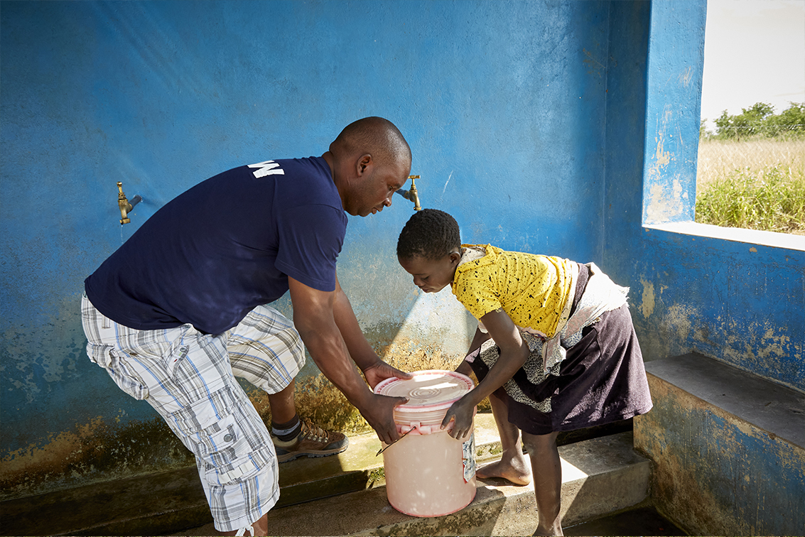 Mada Selenje, liaison officer and agricultural officer at Imani Consultants, the organization which manages the Chikolongo Livelihood Project, together with the community, helps villagers to fill buckets of water with river water pumped from the Shire River.