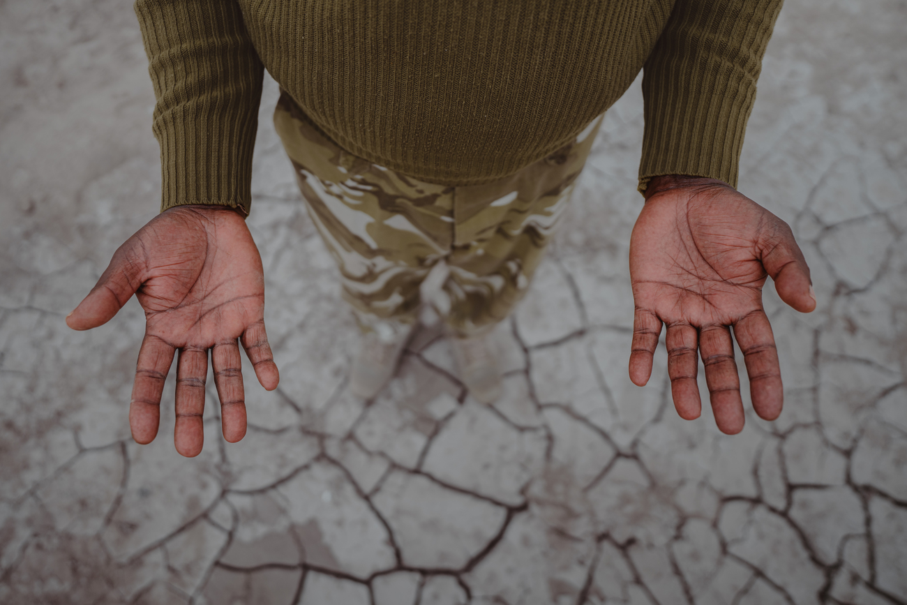 KWS Ranger Samuel Atambo's hands against the dry cracked earth during a drought in Amboseli National Park, Kenya.