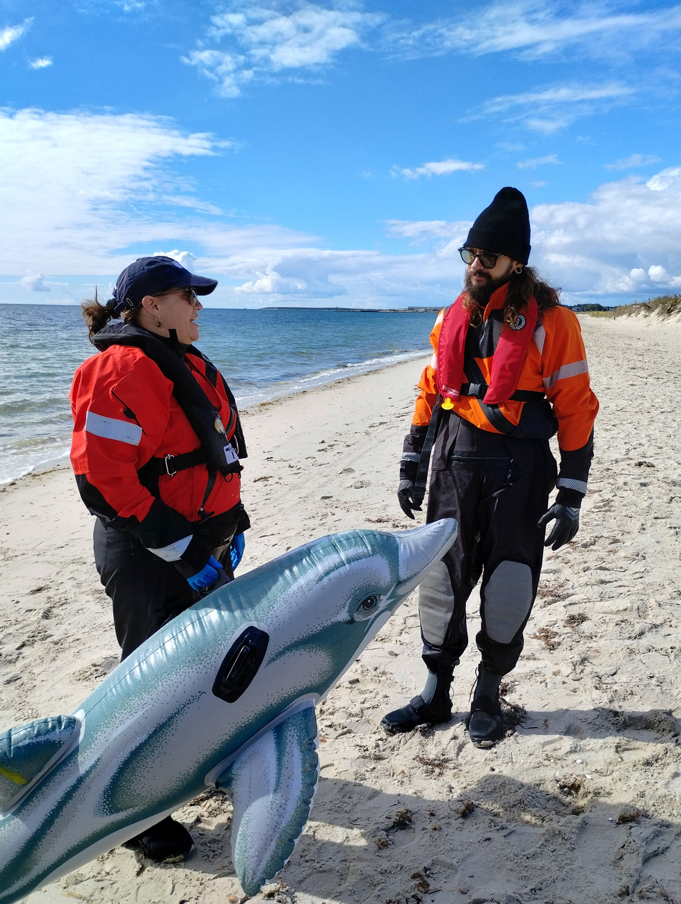 Tom Kaulitz am Strand mit einer IFAW Mitarbeiterin sowie einer Delfinattrappe, die zu Übungszwecken dient.