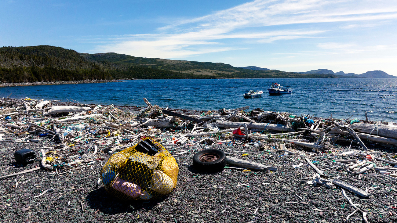 A yellow net holding trash collected during a beach cleanup sits amongst the plastic debris and "ghost gear" still scattered along the shoreline.