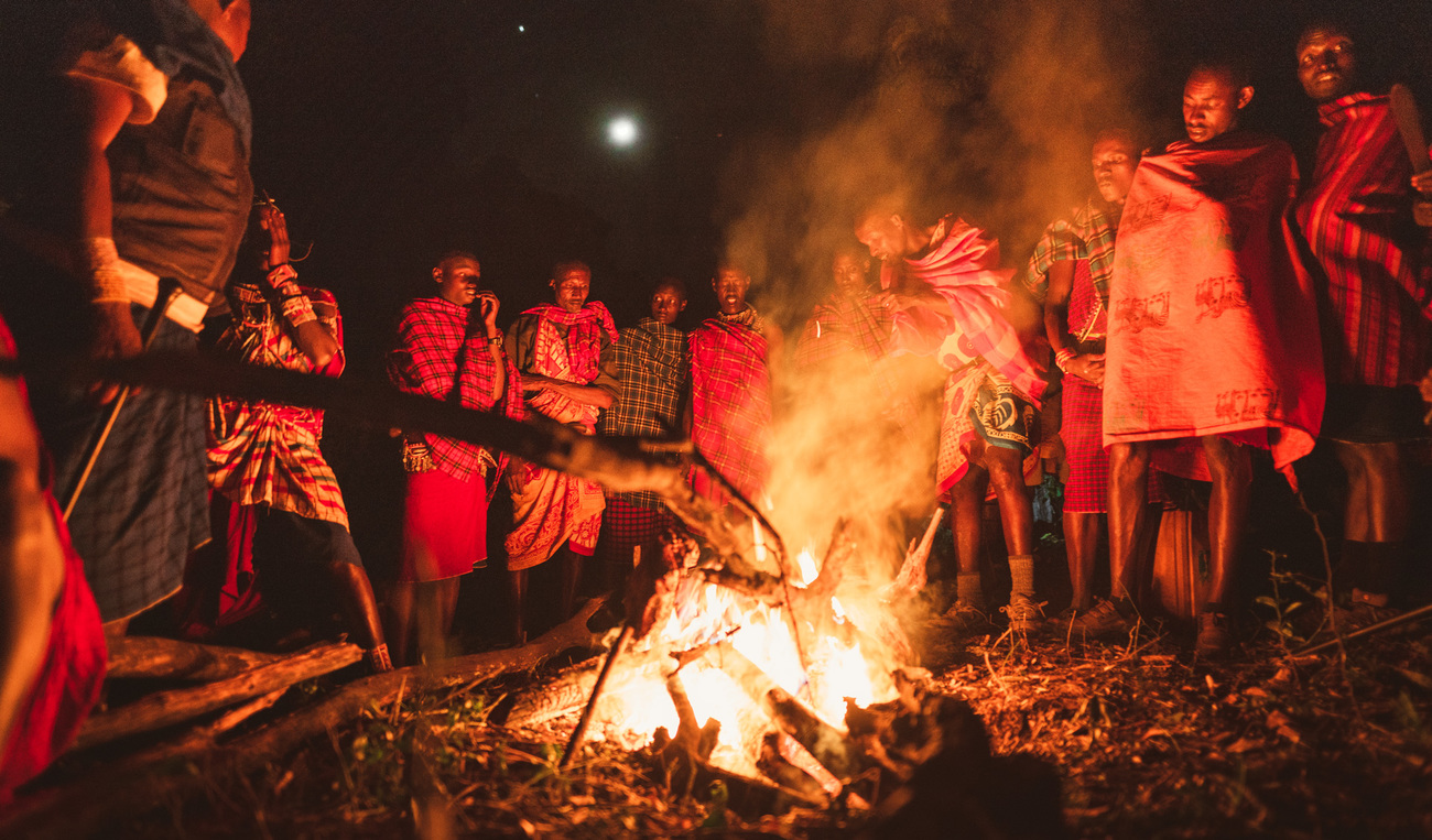 Maasai figureheads stand around an evening campfire in Loita forest, Maasai Mara National Reserve, Kenya.